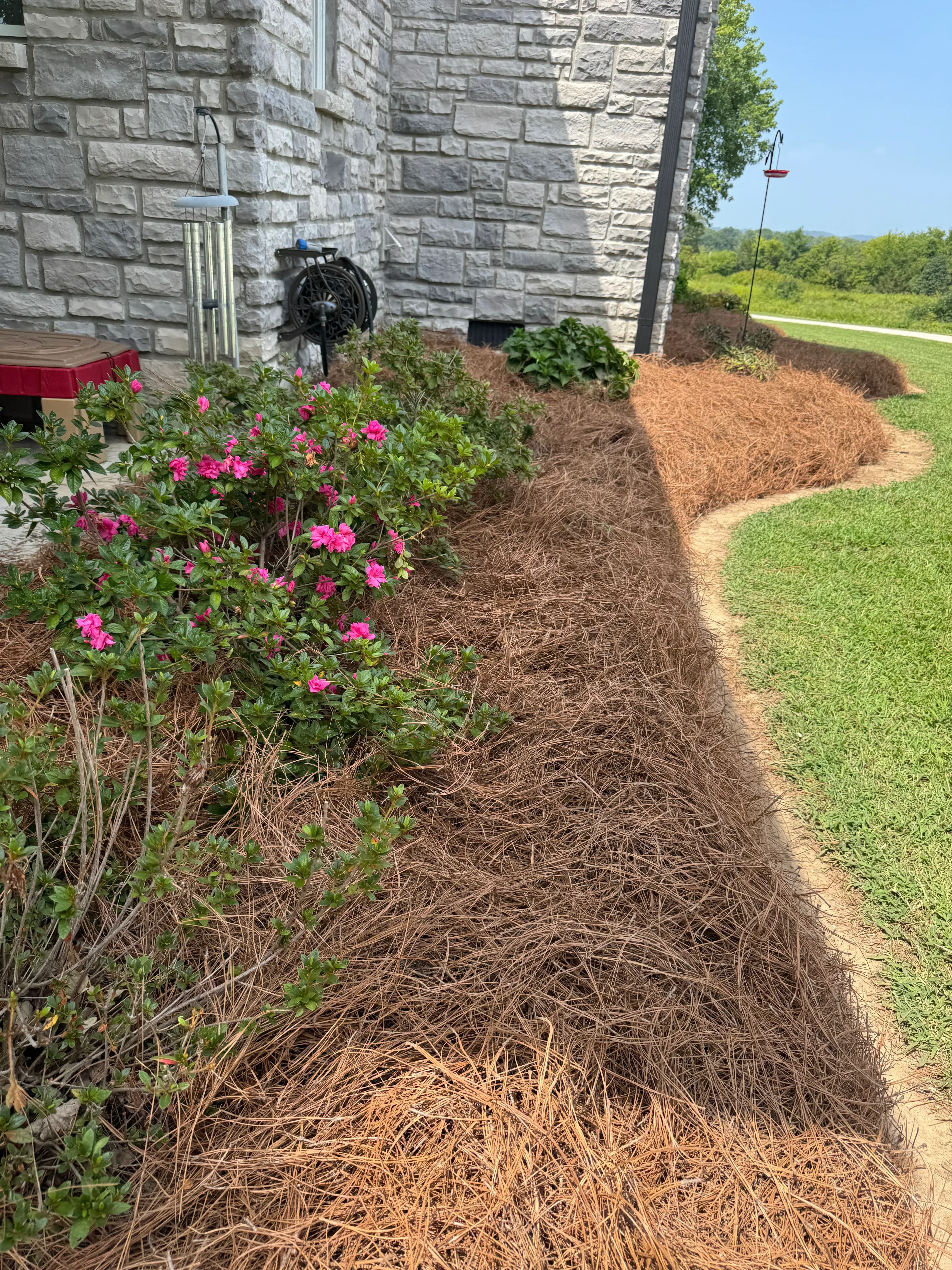 Brown mulch installation in landscape bed with pink flowers and stone retaining wall
