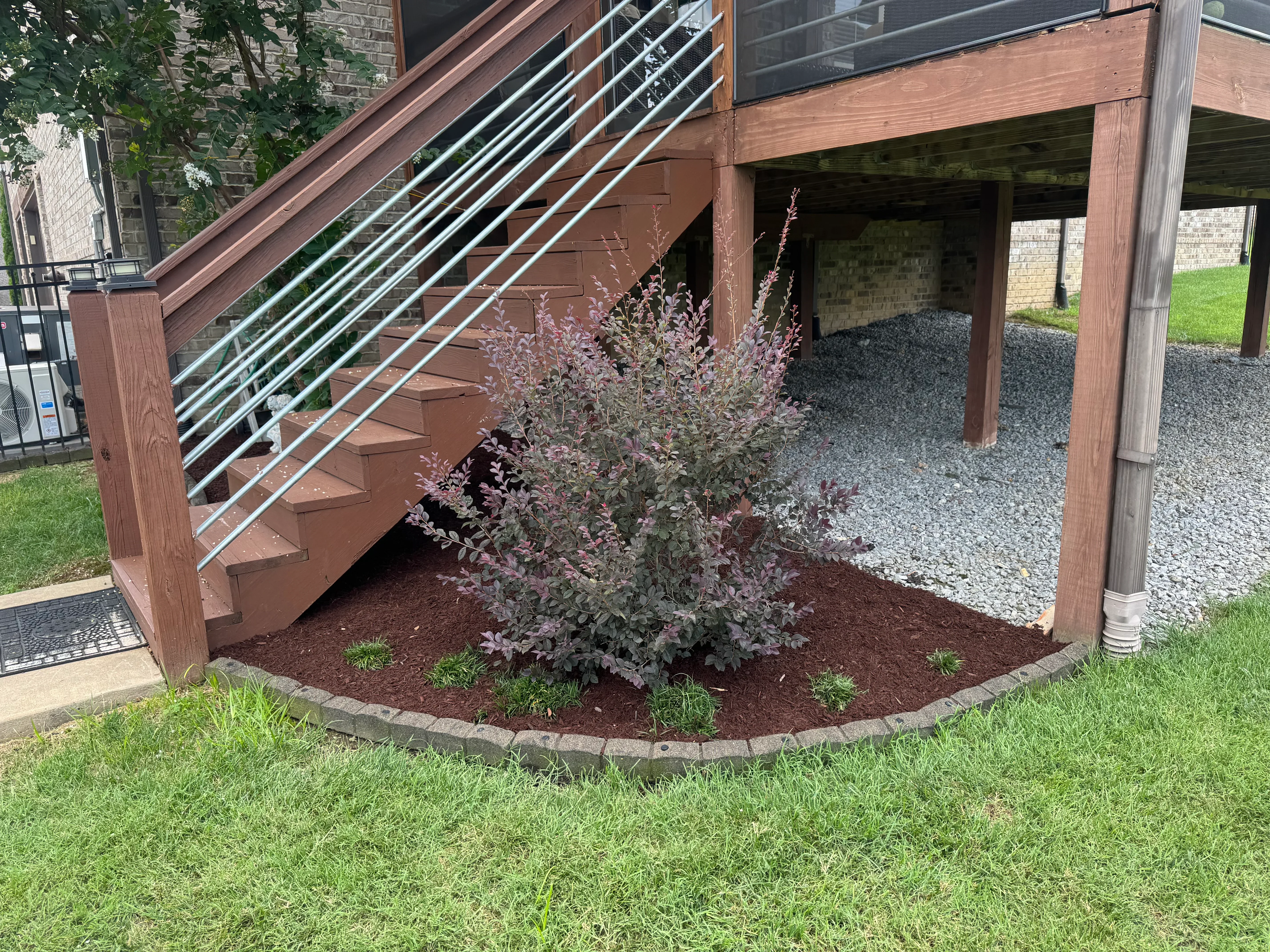 Dark mulch bed with burgundy shrub and stone border under wooden deck
