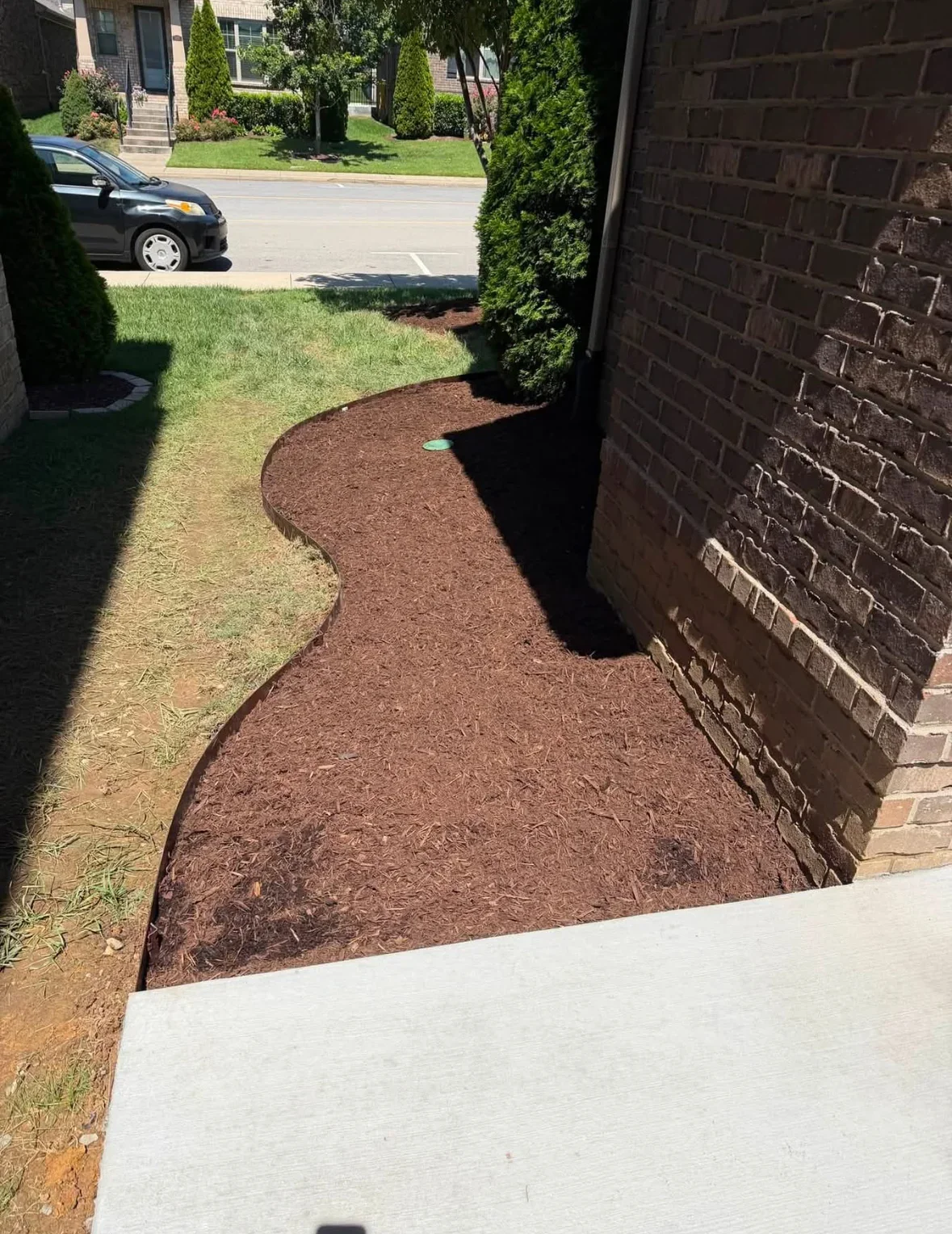 Brown mulch bed with curved edging along brick home foundation and lawn