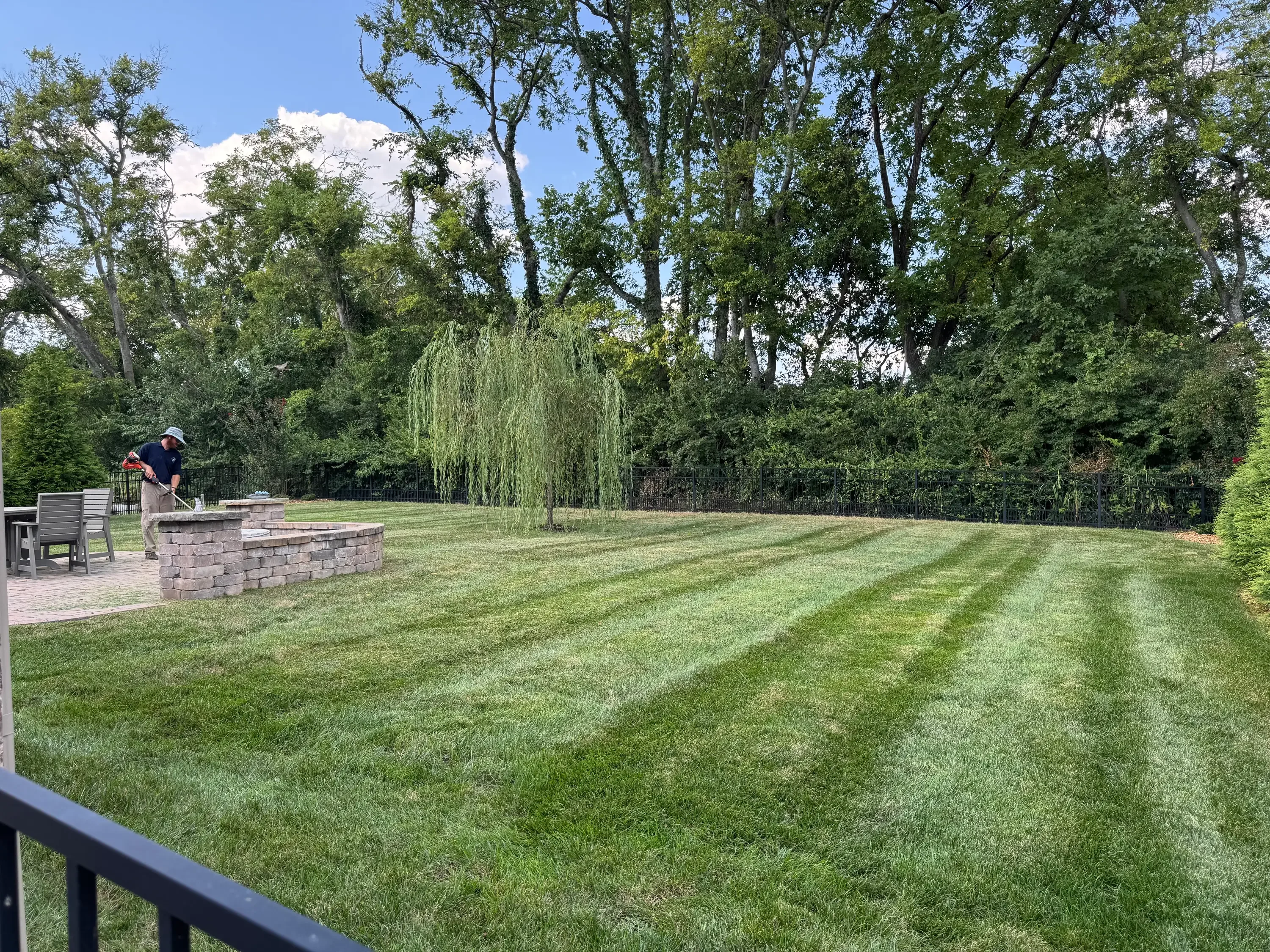 Striped lawn with brick paver patio, stacked stone fire pit, and mature trees